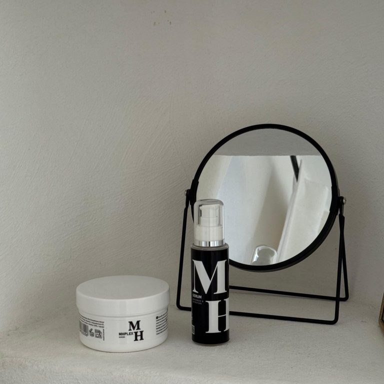 Productos capilares MH Plex Mascarilla y serum sobre una superficie junto a un espejo redondo.